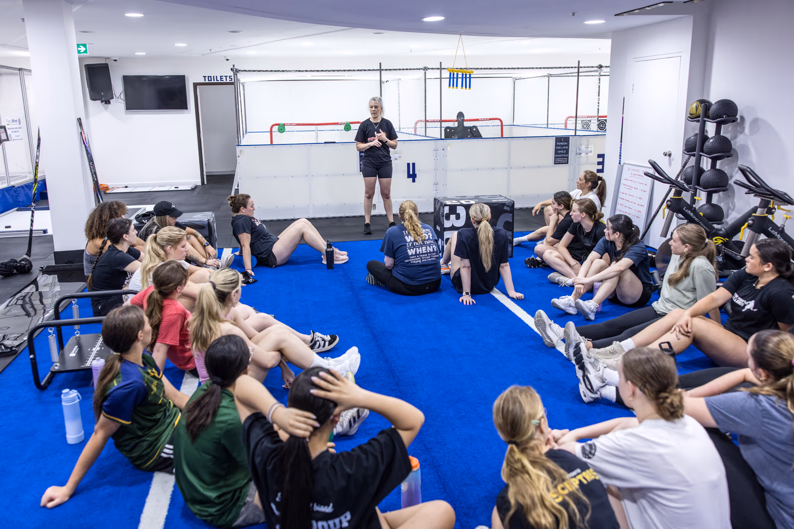 A hockey squad seated on the training floor for a team session with their coach